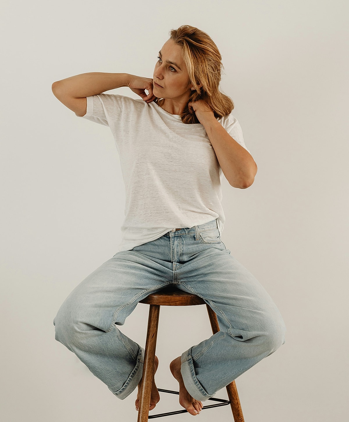 Woman sitting on stool, adjusting hair.